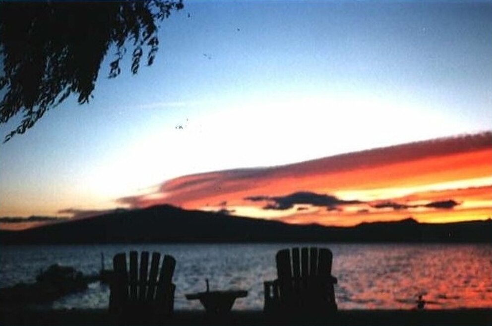 Sunset over Agency Lake with two Adirondack chairs on the lawn