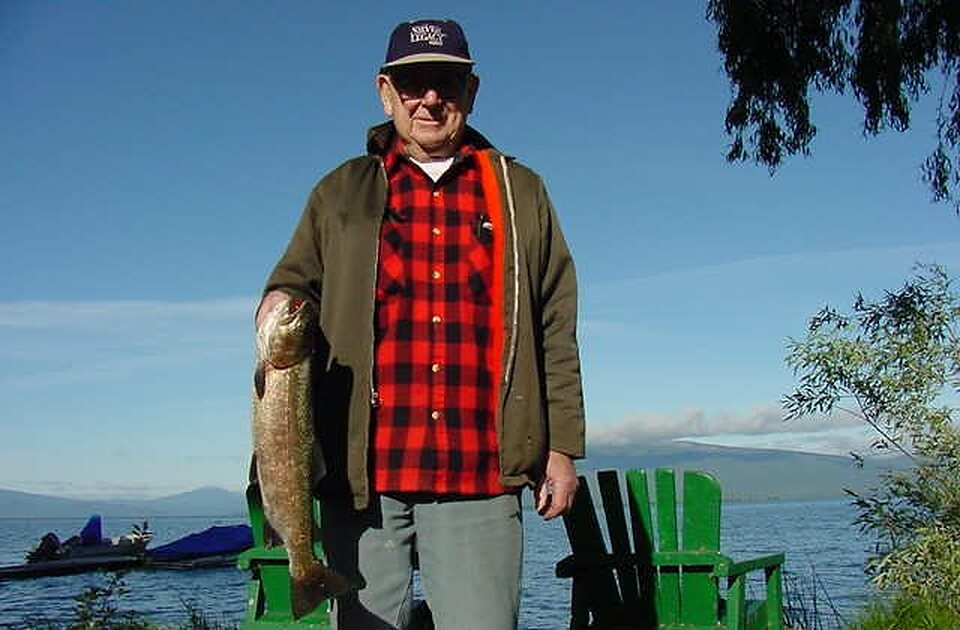 Angler with a big trout beside the lake and green Adirondack chairs