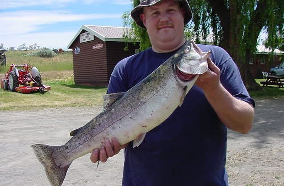 Angler holding a big trout in front of a cabin