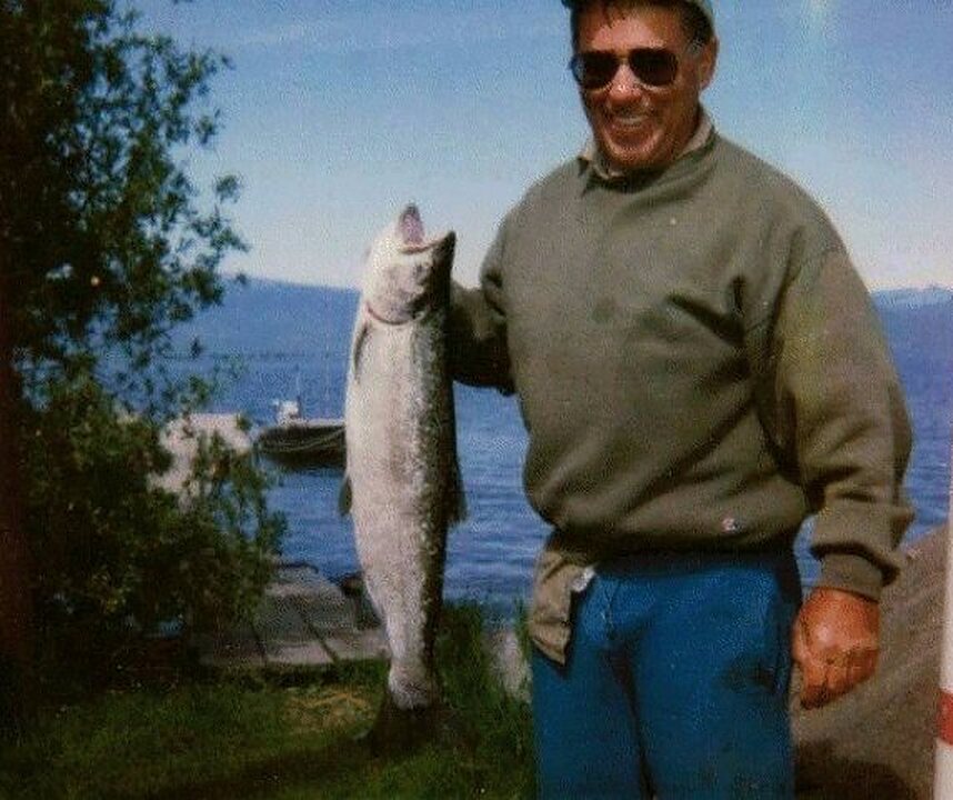 Smiling angler with a long trout by the water